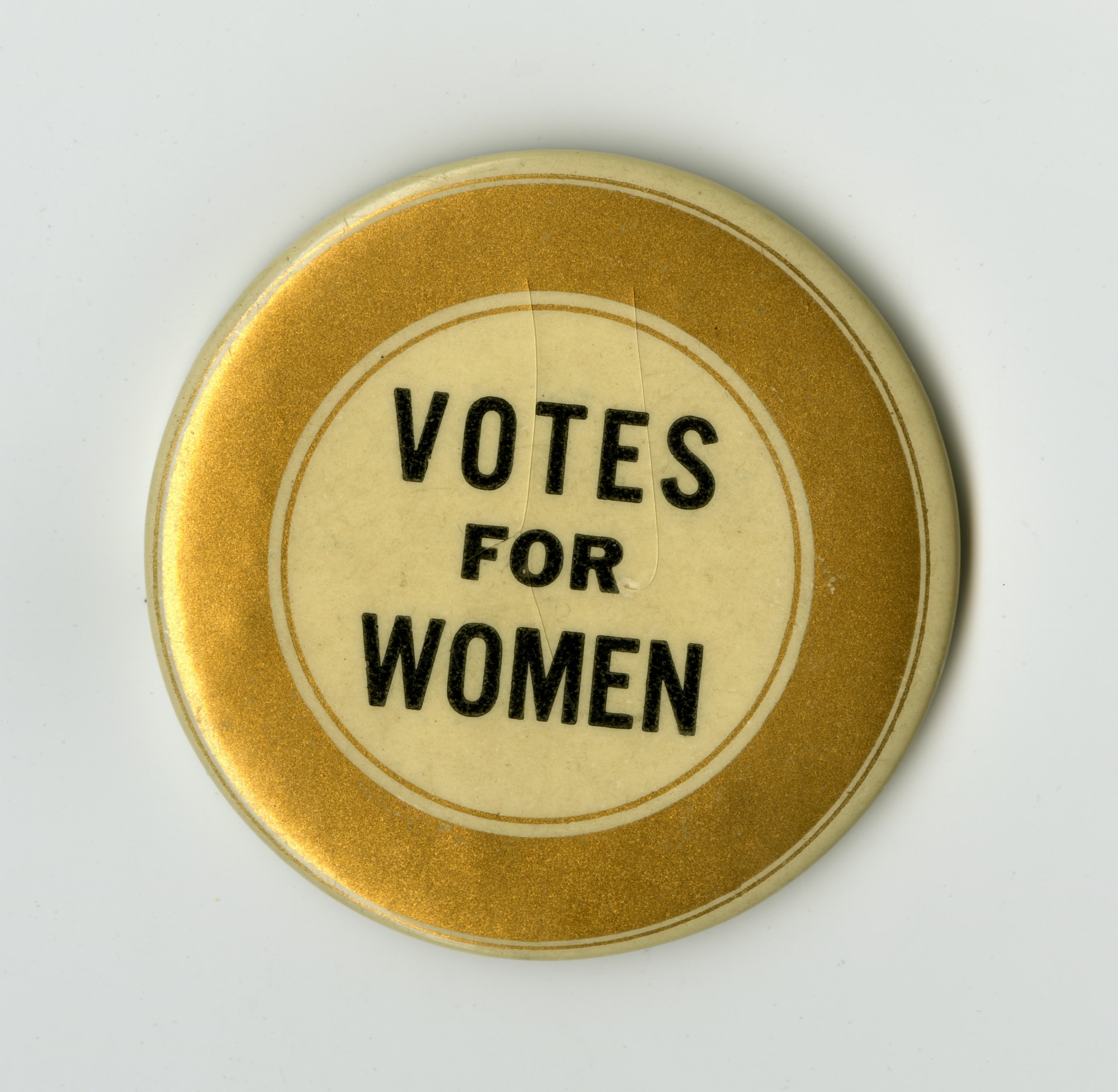 Color photo of a button from the early 1900s supporting women's suffrage that says "Votes for Women" in black text surrounded by a gold circle border; Public domain image, courtesy of RawPixel.com